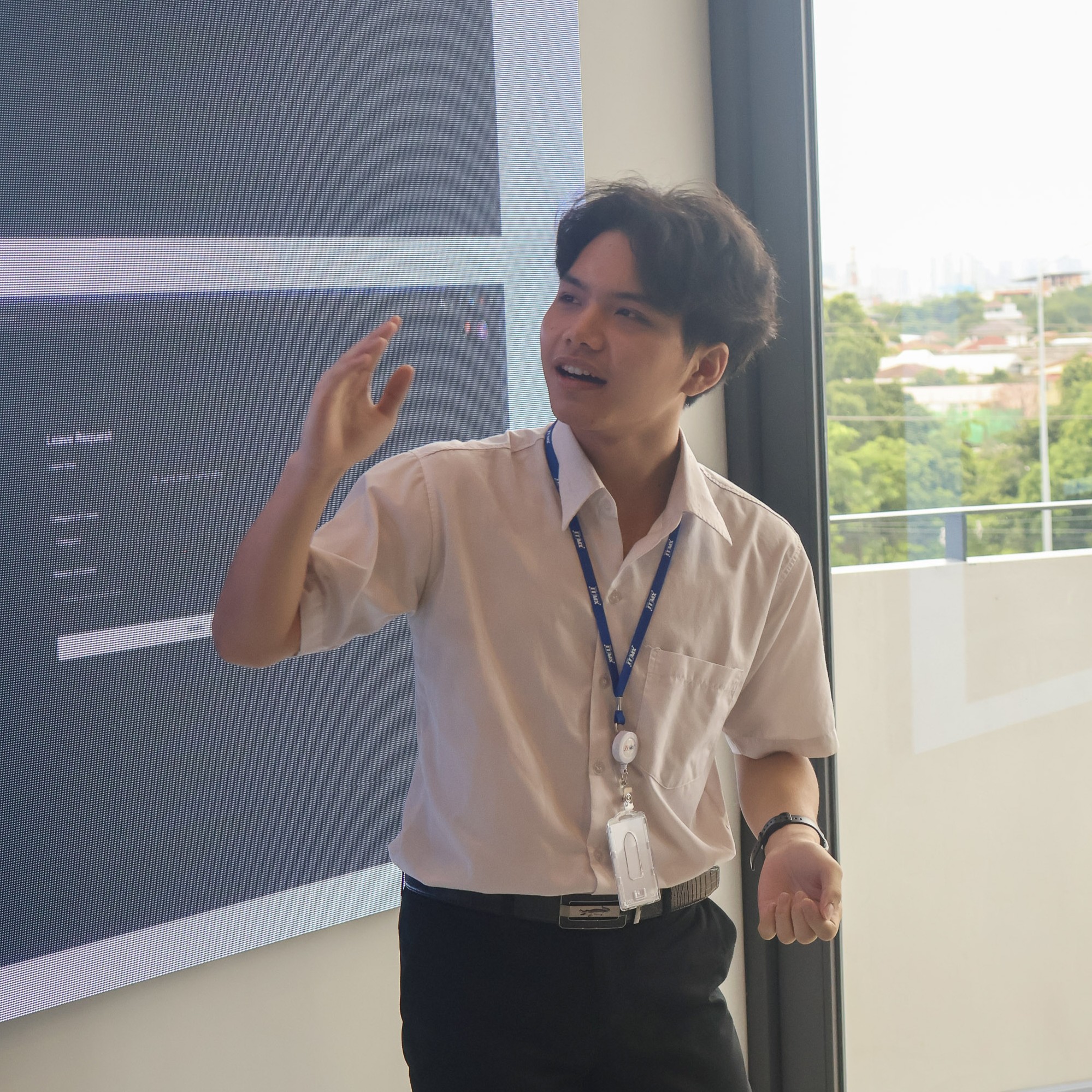 Pasit Khumsena presenting at a tech event, gesturing while explaining concepts next to a display screen